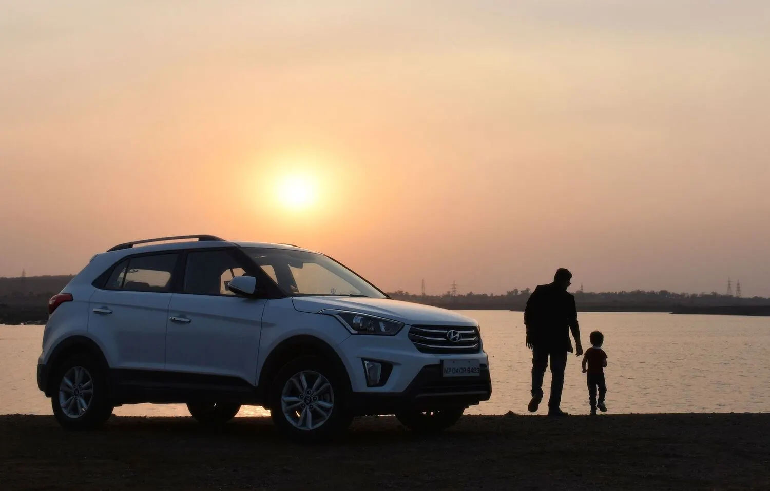 White Hyundai Creta parked by a lake at sunset, with a father and young son walking beside it