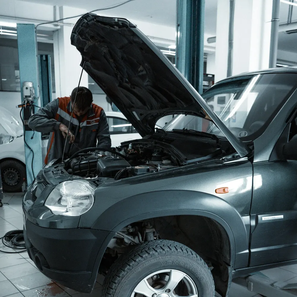 Mechanic working under the open bonnet of a grey 4x4 in a garage workshop